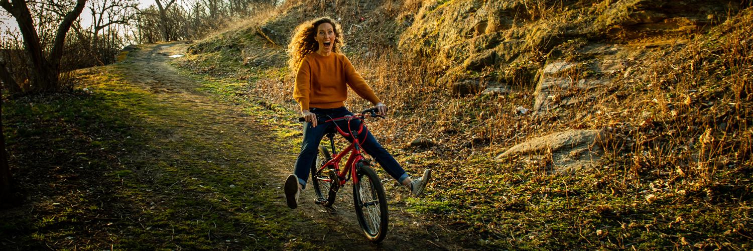 A young woman with red hair careens down a hill on a too-small red BMX bike. Photo: Wide Eyed Studios