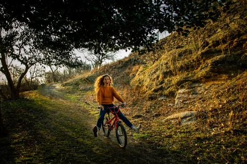 A young woman with red hair careens down a hill on a too-small red BMX bike. Photo: Wide Eyed Studios